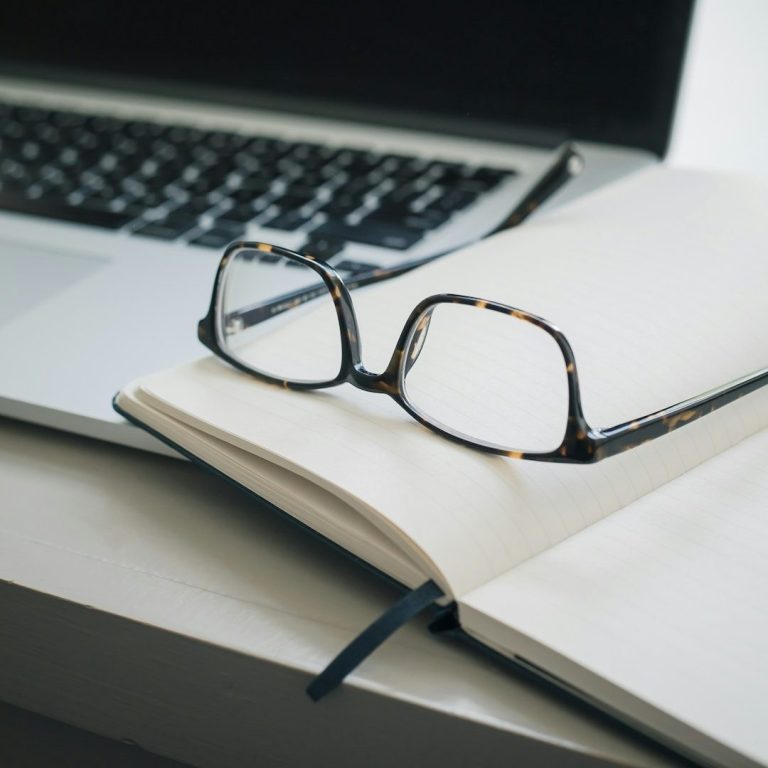 Brille liegt auf einem offenen Notizbuch neben einem Laptop.