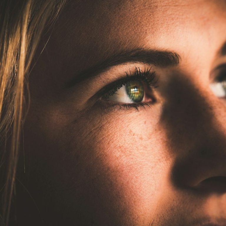 Nahaufnahme eines menschlichen Auges mit grüner Iris und weichem Licht.