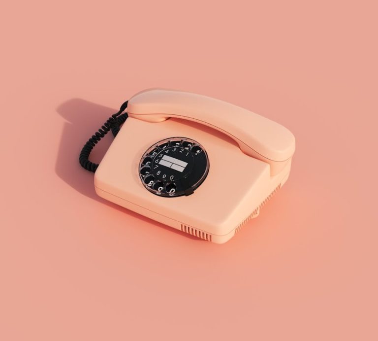 Rosafarbenes Retro-Telefon mit Wahlscheibe vor einem rosafarbigen Hintergrund.