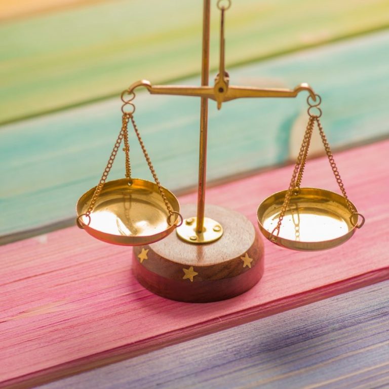 Bild einer einer goldenen Waage auf einem bunten Holztisch.