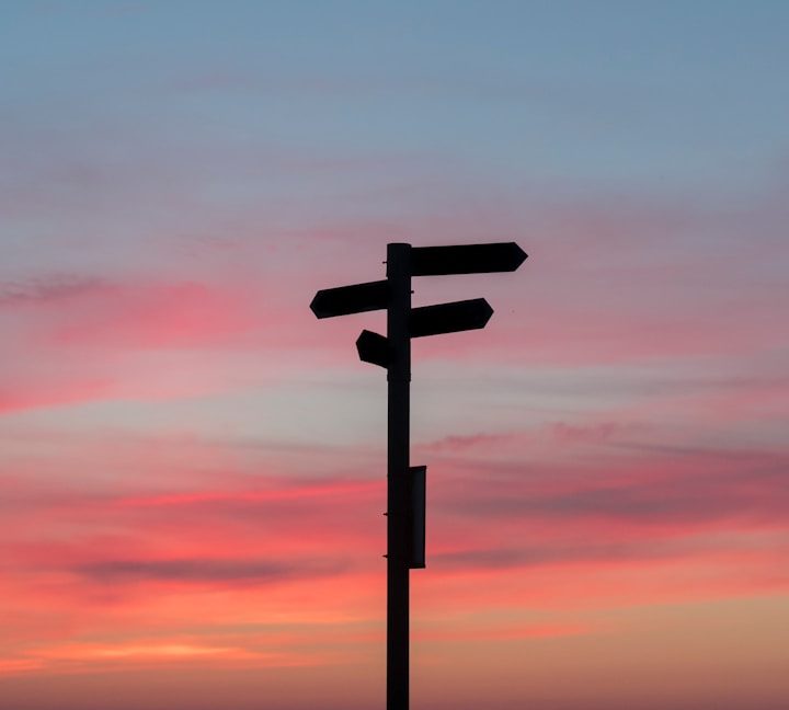 Wegweiser vor einem bunten Sonnenuntergang mit pinkem und blauen Himmel.