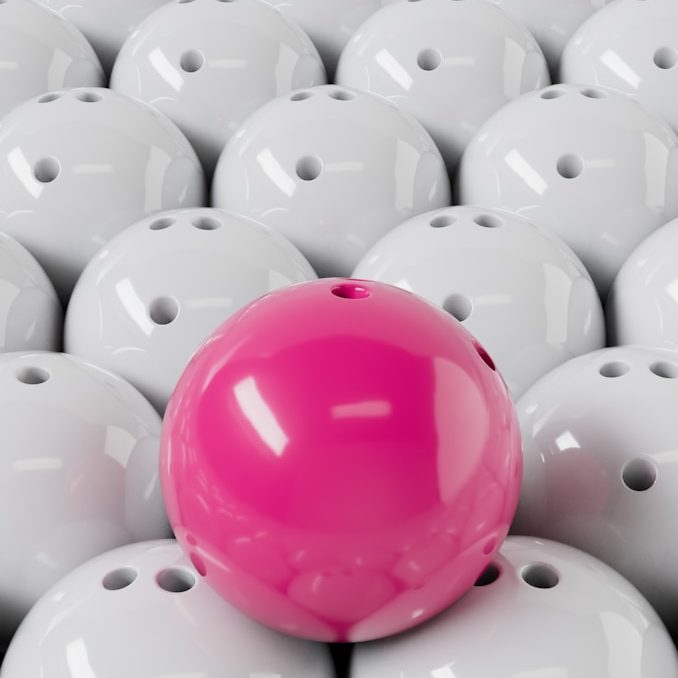 Bild einer pinkfarbenen Bowlingkugel zwischen vielen weißen Bowlingkugeln.